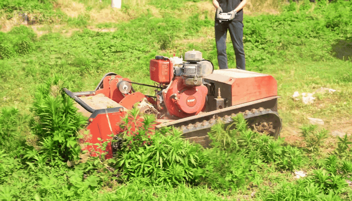 The front cutting head clears weeds as the mower advances, supporting routine maintenance of green spaces with unwanted vegetation.