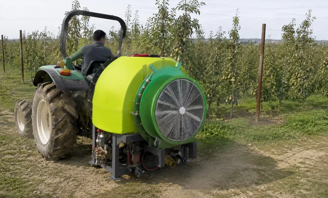 A levegővel segített permetezés a körtefa belső ágaira is eljut, miközben a traktor egyenletesen halad a sorok között.