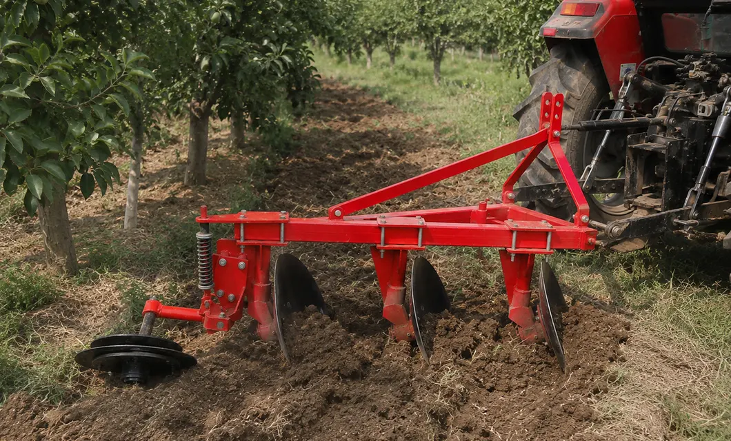 Eine Szene in einer Obstbaumreihe zeigt drei Scheiben, die hinter einem Traktor zwischen den Bäumen den Boden bearbeiten.
