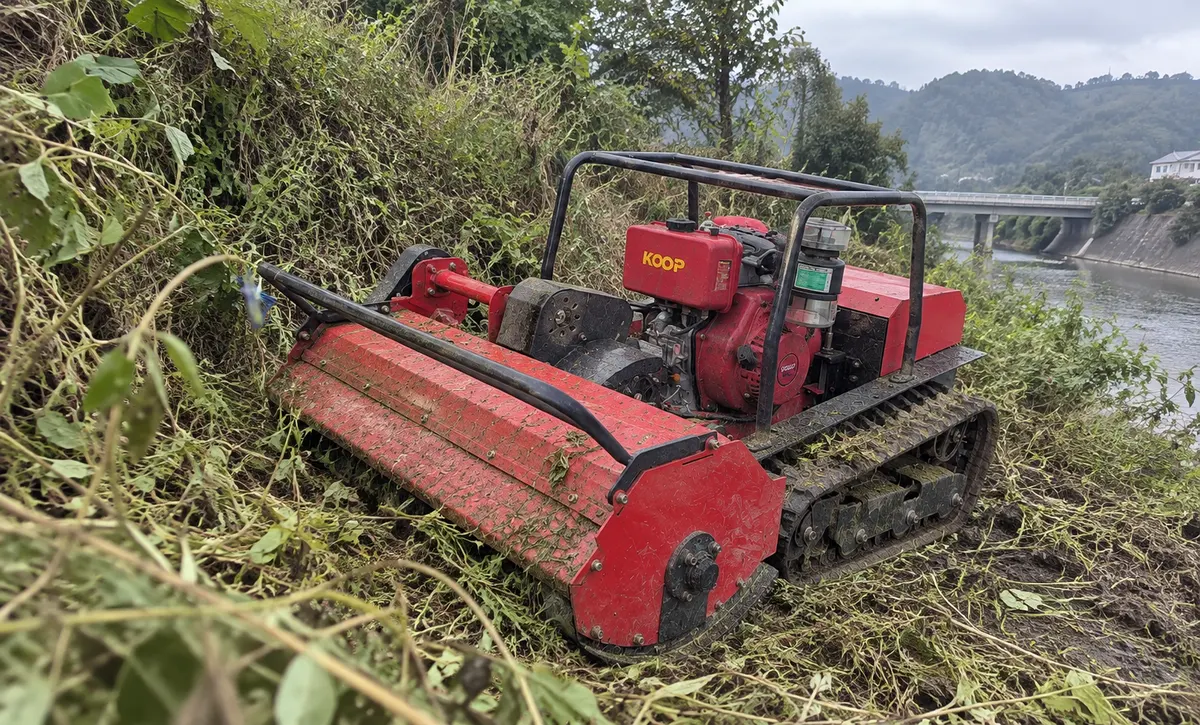 The mower clears dense weeds along a steep riverbank with ease.