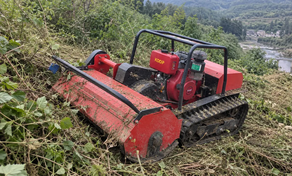 The tracked unit cuts thick brush across rough and sloped terrain.